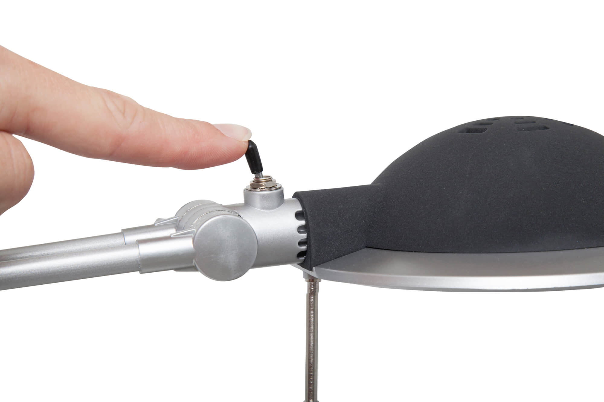 Ręka dotykająca włącznika/wyłącznika srebrnej i czarnej lampy biurkowej.