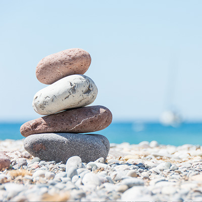 Stapel aus vier Steinen an einem Strand mit Ozean und Himmel im Hintergrund.