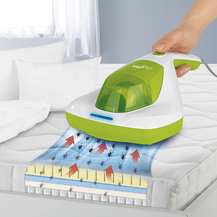 Una mano tiene un aspirapolvere verde e bianco per letto sopra un materasso, con frecce che indicano la pulizia.
