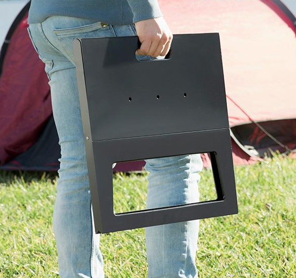 Persona che tiene una griglia nera. Tenda rossa sullo sfondo, erba verde.