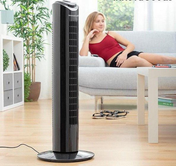 Eine Frau in rotem Tanktop liegt auf einer Couch, in der Nähe eines schwarzen Turmventilators und eines weißen Tisches.