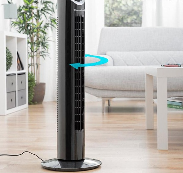 Schwarzer Turmventilator in einem Wohnzimmer, mit Sofa und Tisch im Hintergrund.