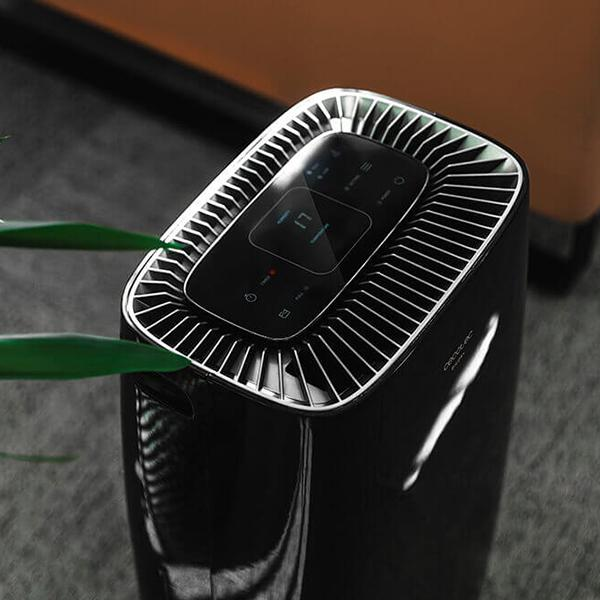 Czarny oczyszczacz powietrza z panelem sterowania, liśćmi z przodu i rozmytym tłem.