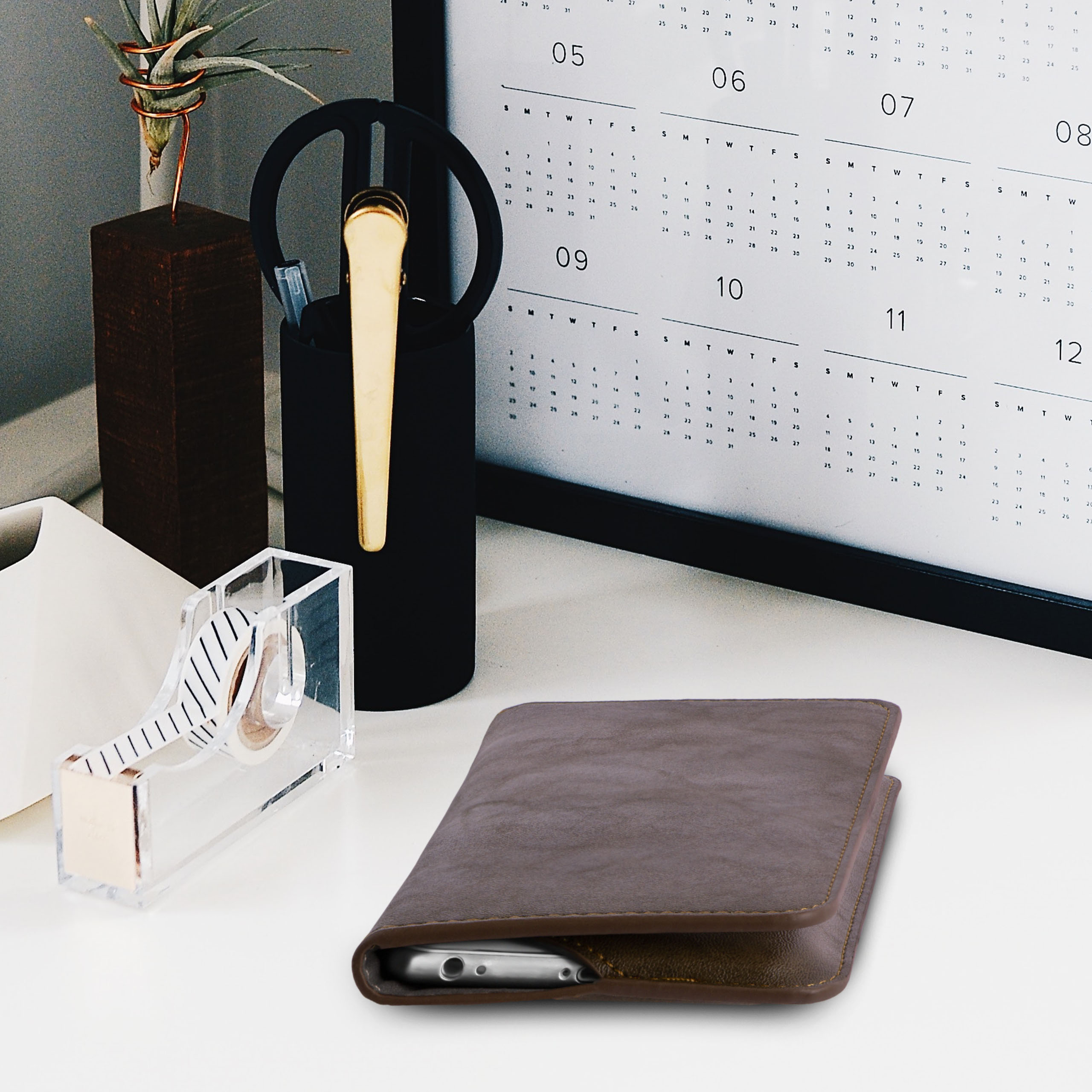 Schreibtisch mit: Handyhülle, Klebebandspender, Stifthalter, Kalender. In der Hülle ist ein Handy.