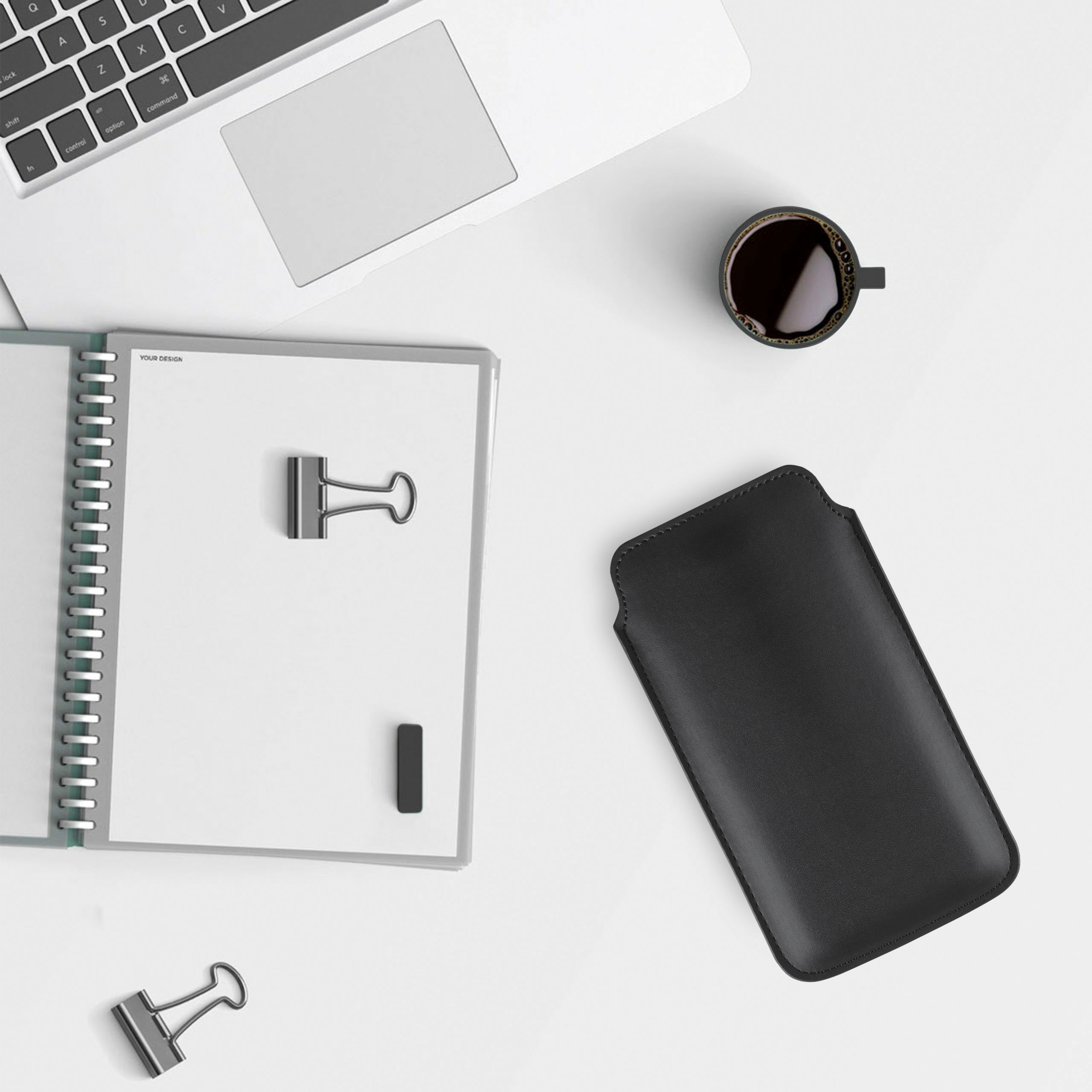 Arbeitsplatz: Laptop, Notizbuch, Kaffee und schwarze Handytasche.