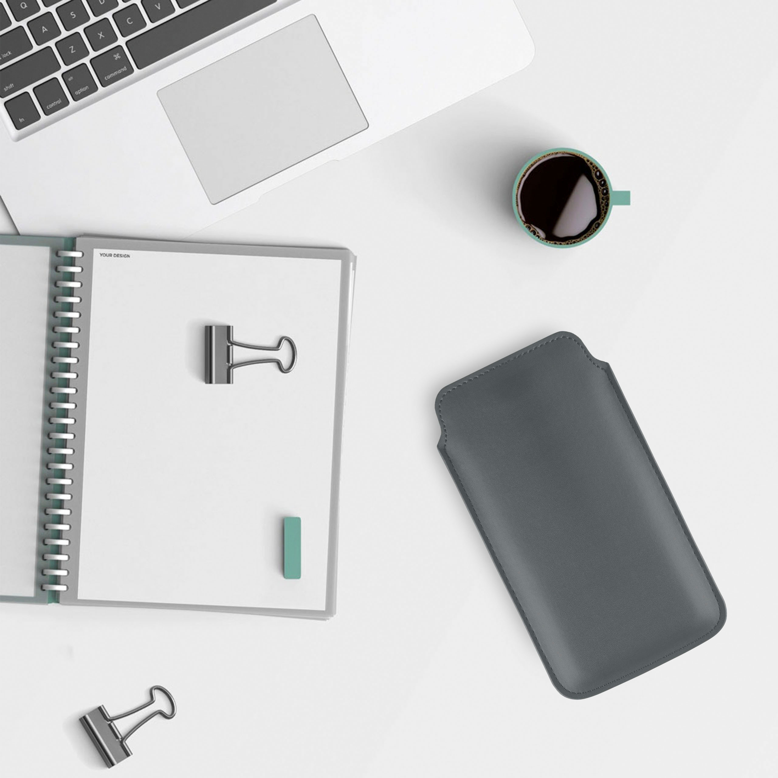 Laptop, Notizbuch und Stift auf weißem Schreibtisch. Graue Handyhülle und Büroklammern.
