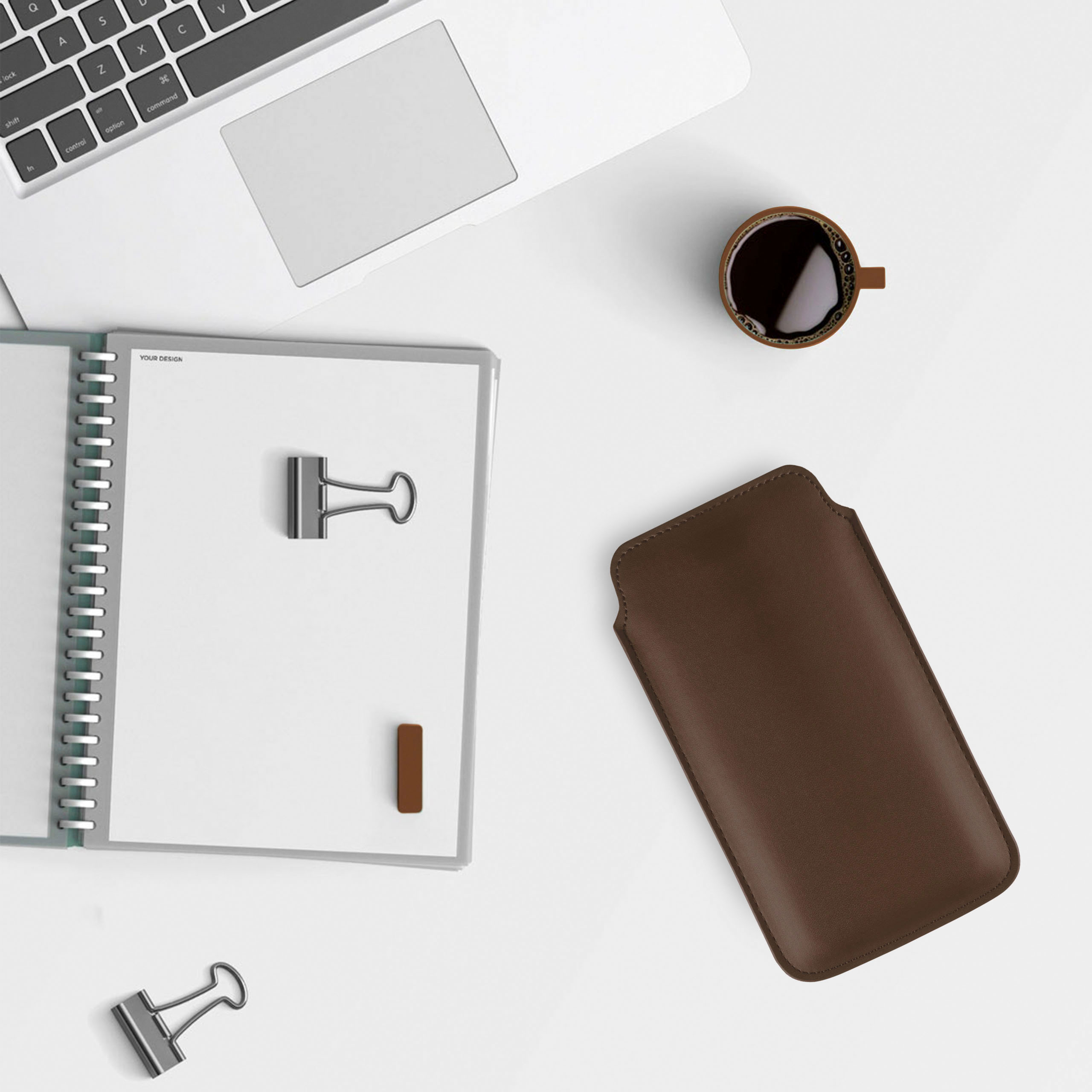 Ein Schreibtisch mit Laptop, Notizbuch, Kaffeetasse, Handyhülle und zwei Büroklammern. Draufsicht.