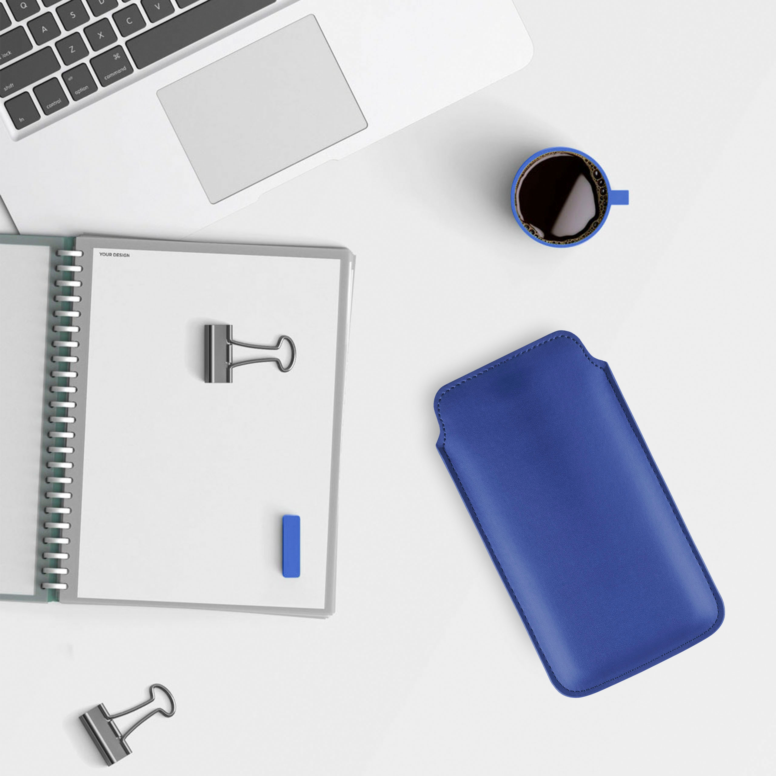Schreibtisch mit Notizbuch, Stiften, Kaffeetasse und blauem Handycase. Draufsicht.