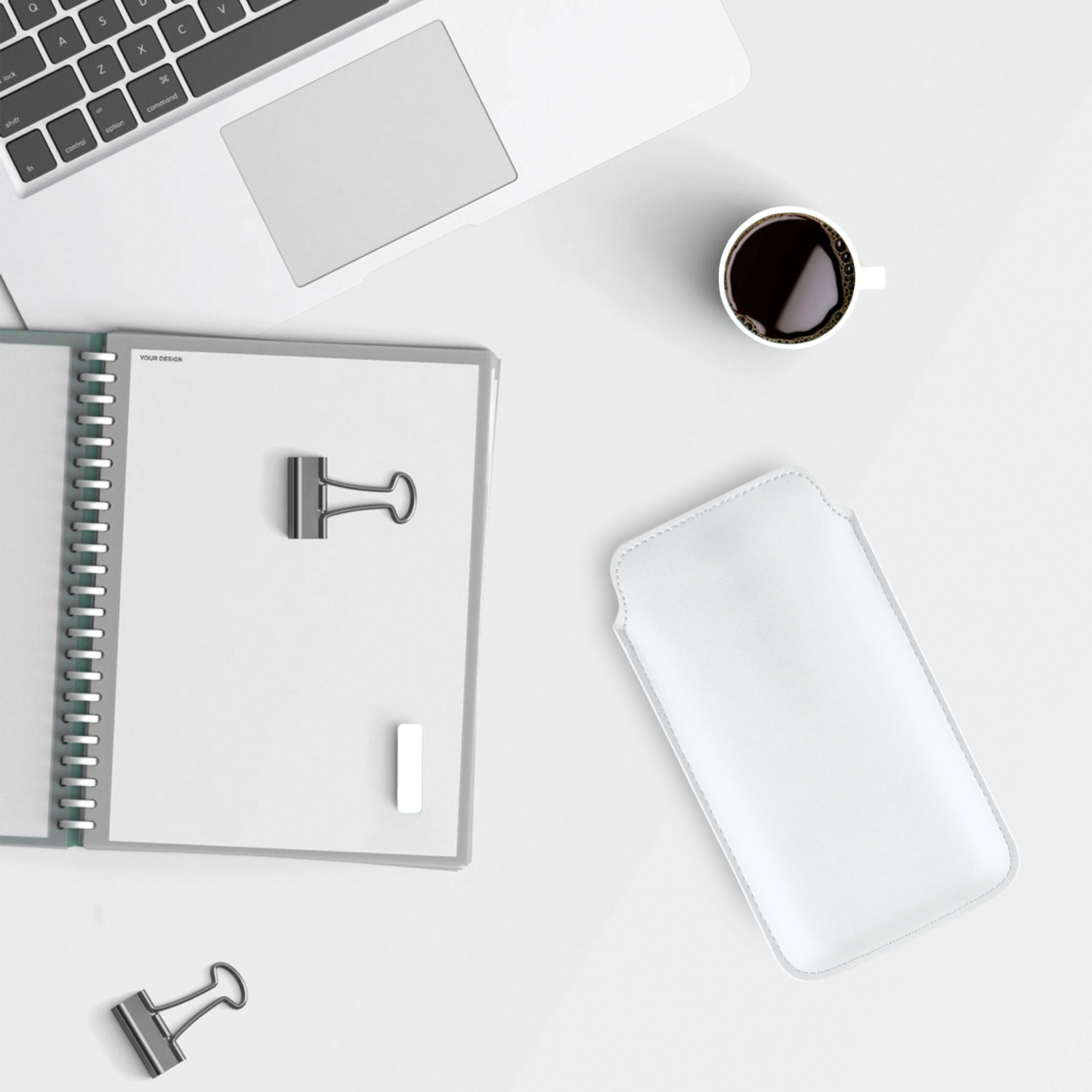 Laptop, Notizbuch und Kaffee auf einem weißen Schreibtisch mit weißer Handyhülle.