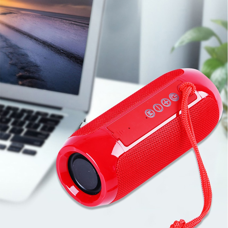 Ein roter, zylindrischer Lautsprecher mit Knöpfen und Trageriemen steht auf einem Tisch neben einem Laptop.