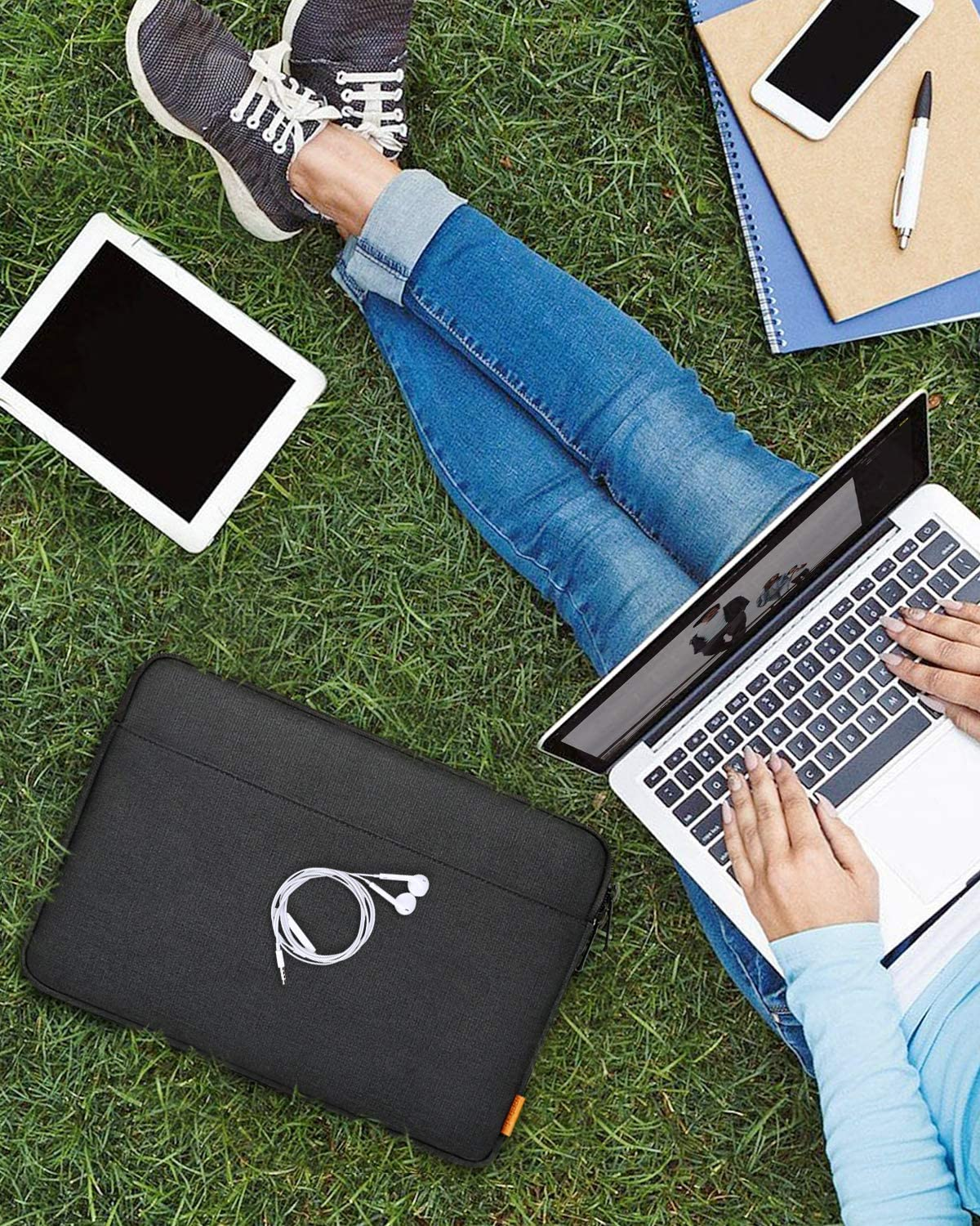 Person am Laptop auf Gras. Tablet und Handy auf Gras. Kopfhörer und Hülle liegen daneben.