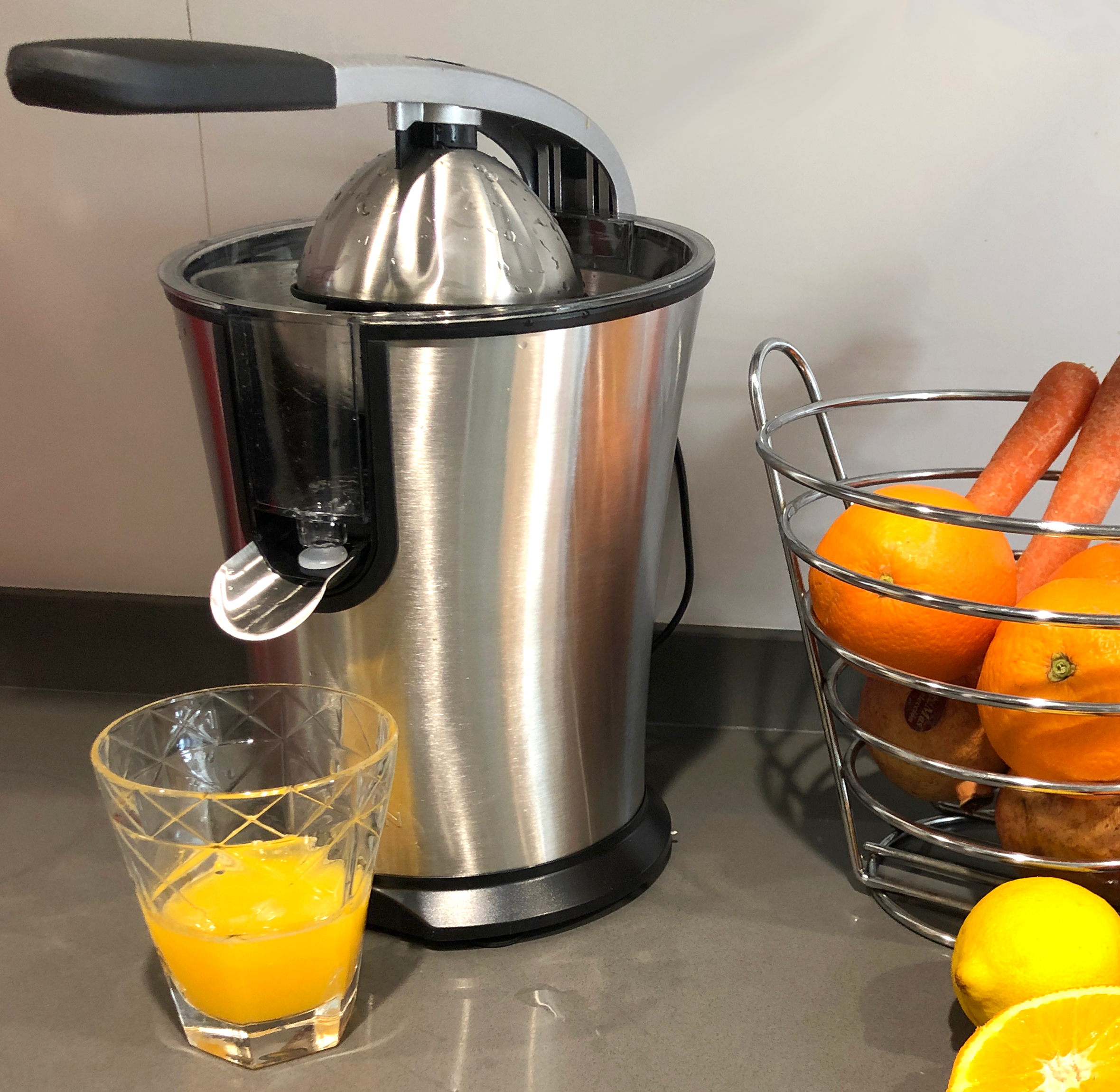 Wyiskarka ze stali nierdzewnej z sokiem pomarańczowym w szklance i koszem owoców na blacie.