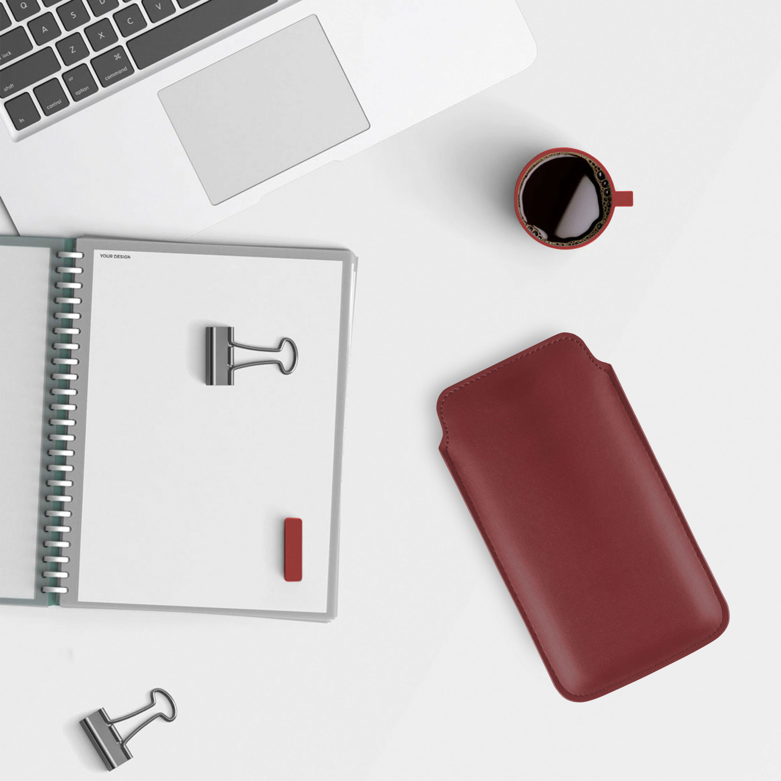 Schreibtisch mit Laptop, Notizbuch, Büroklammern, Kaffeetasse und Handyhülle.