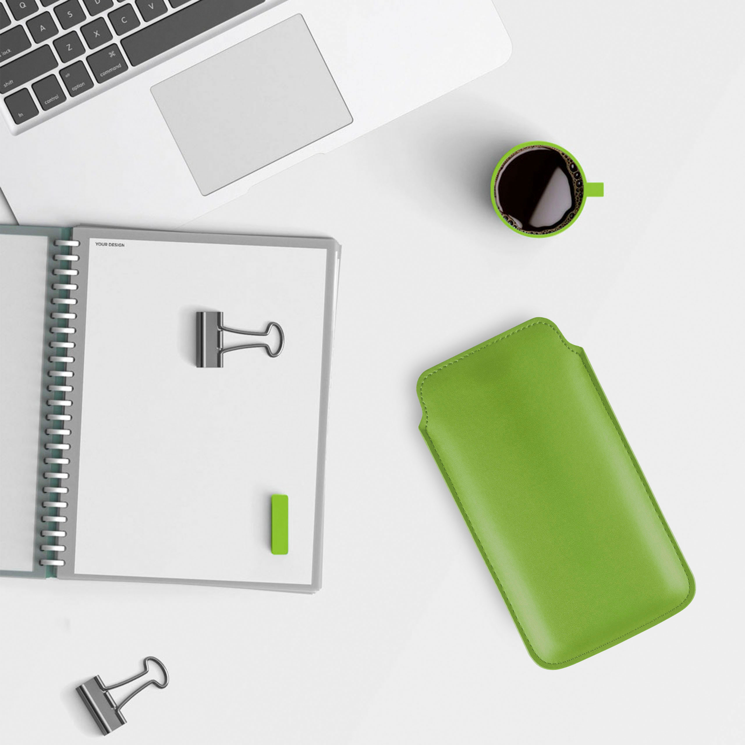 Ein Arbeitsplatz mit Notizbuch, grüner Handyhülle, Kaffeetasse und Zubehör.