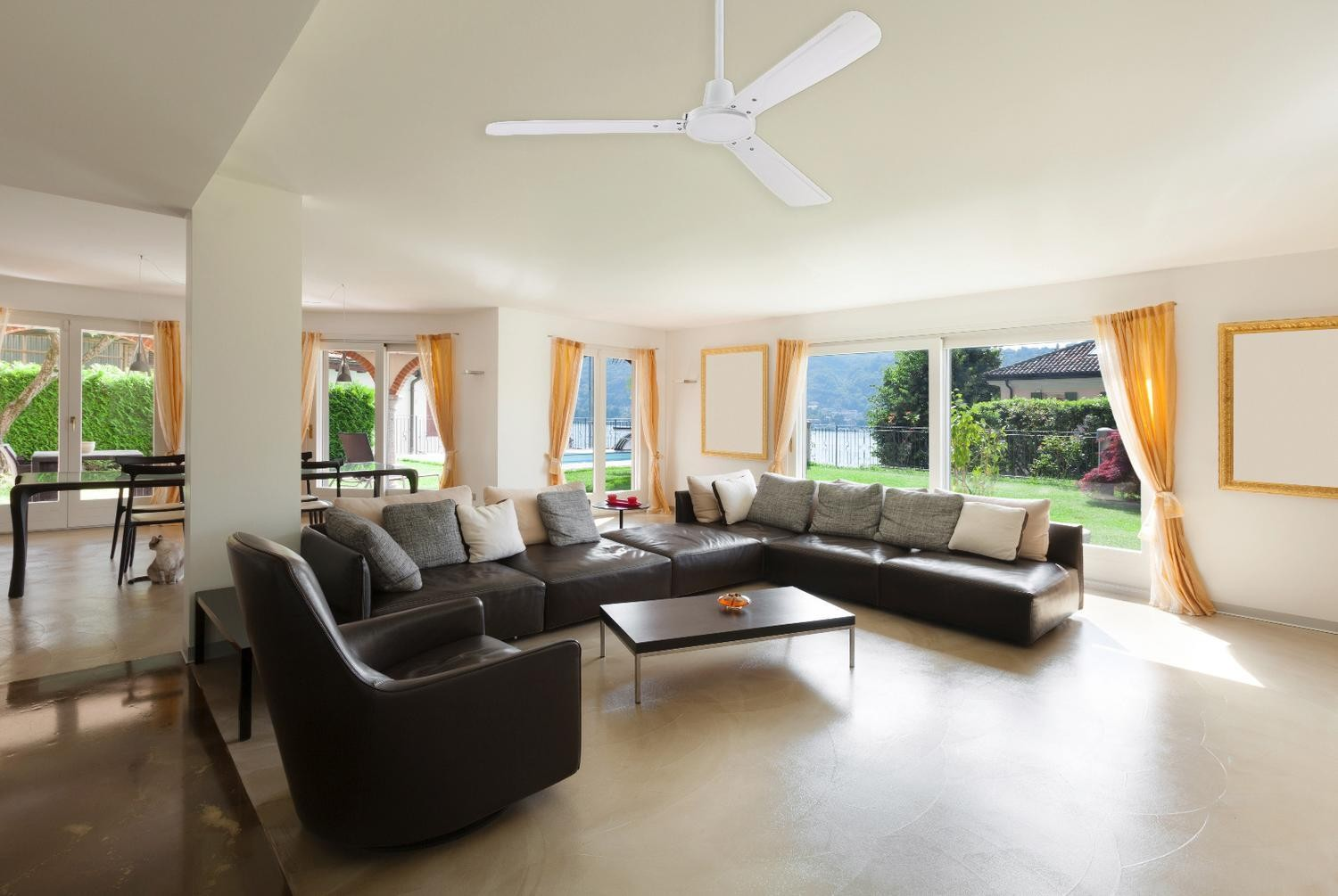 Geräumiges Wohnzimmer mit weißen Wänden, dunkelbraunem Sofa und Deckenventilator. Große Fenster.