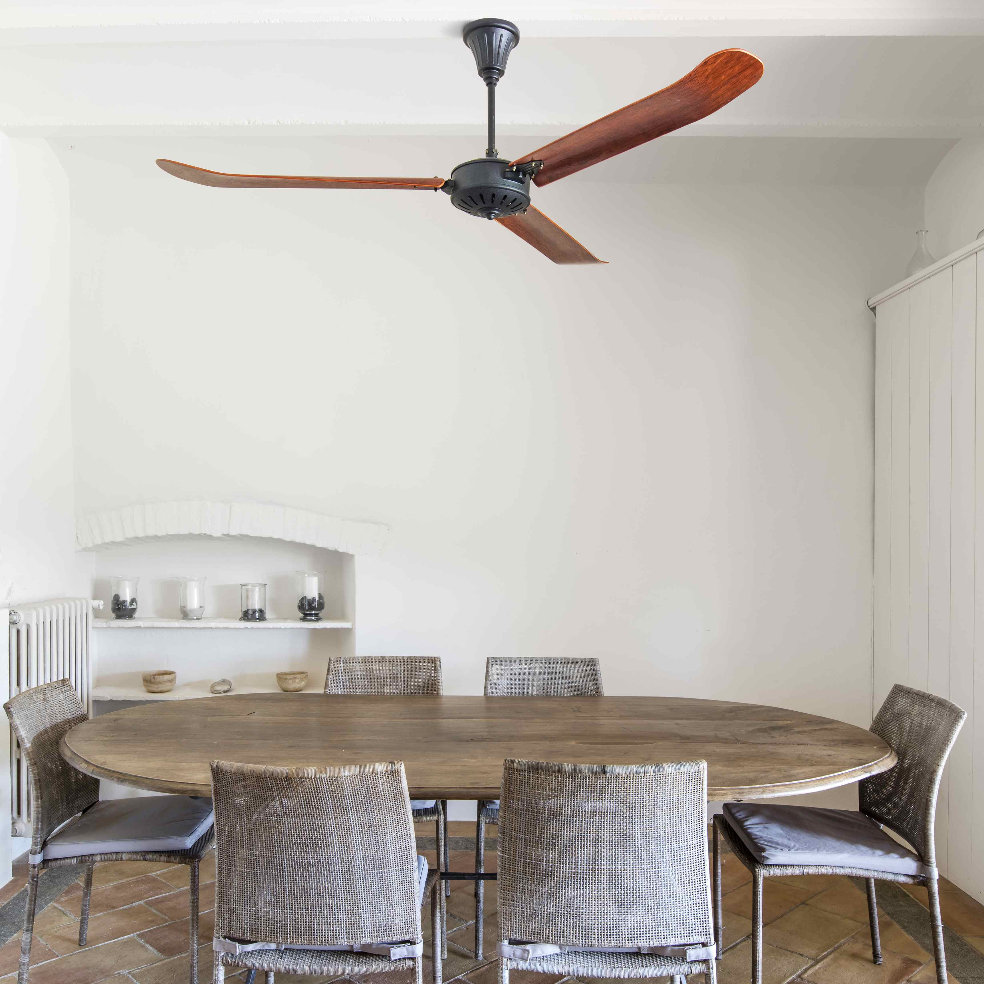 Ein Esszimmer mit einem langen Holztisch, sechs Stühlen und einem Deckenventilator. Weiße Wände und Fliesenboden.