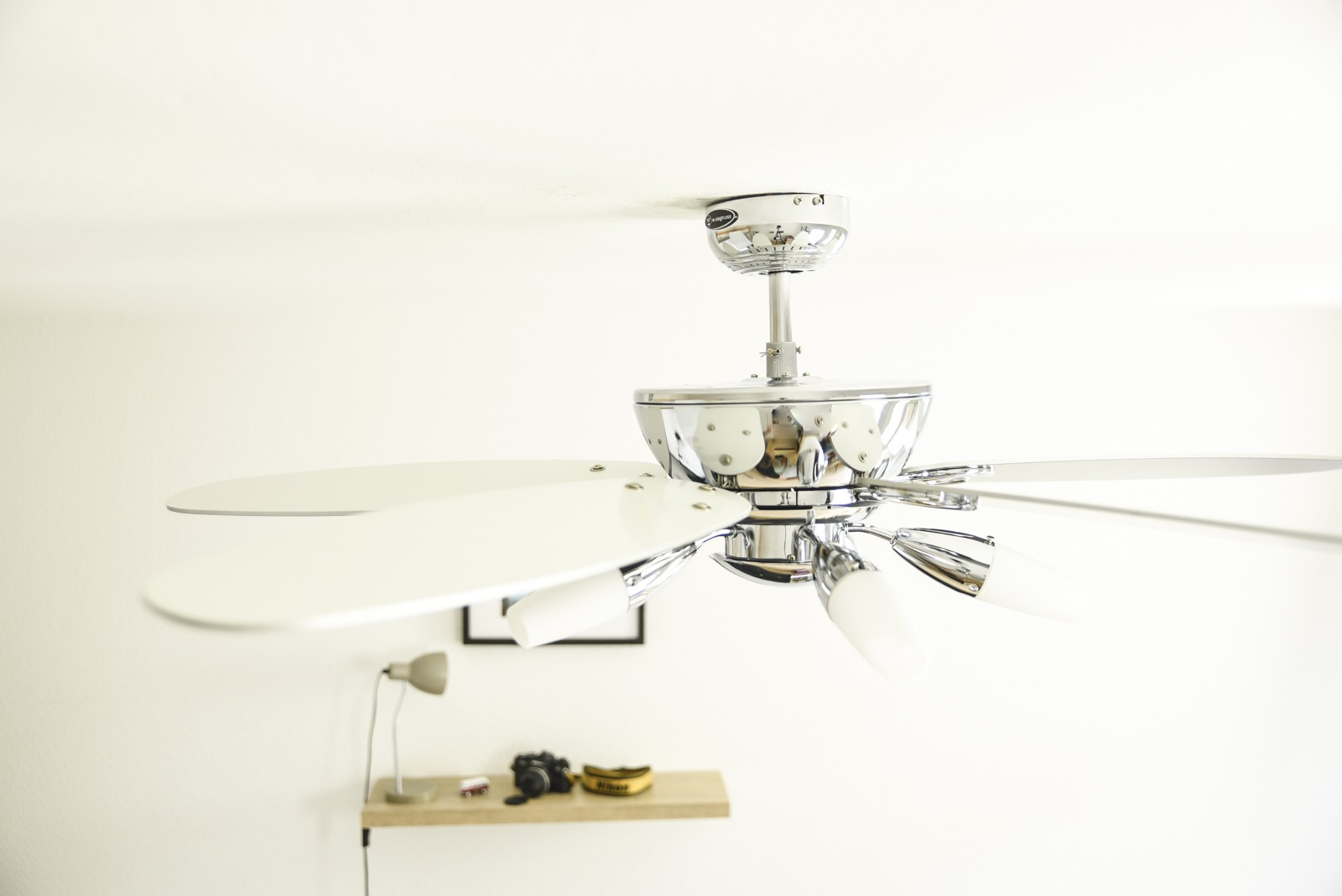 Deckenventilator mit weißen Flügeln und silbernem Motor. Hintergrund ist weiße Decke und Wand.