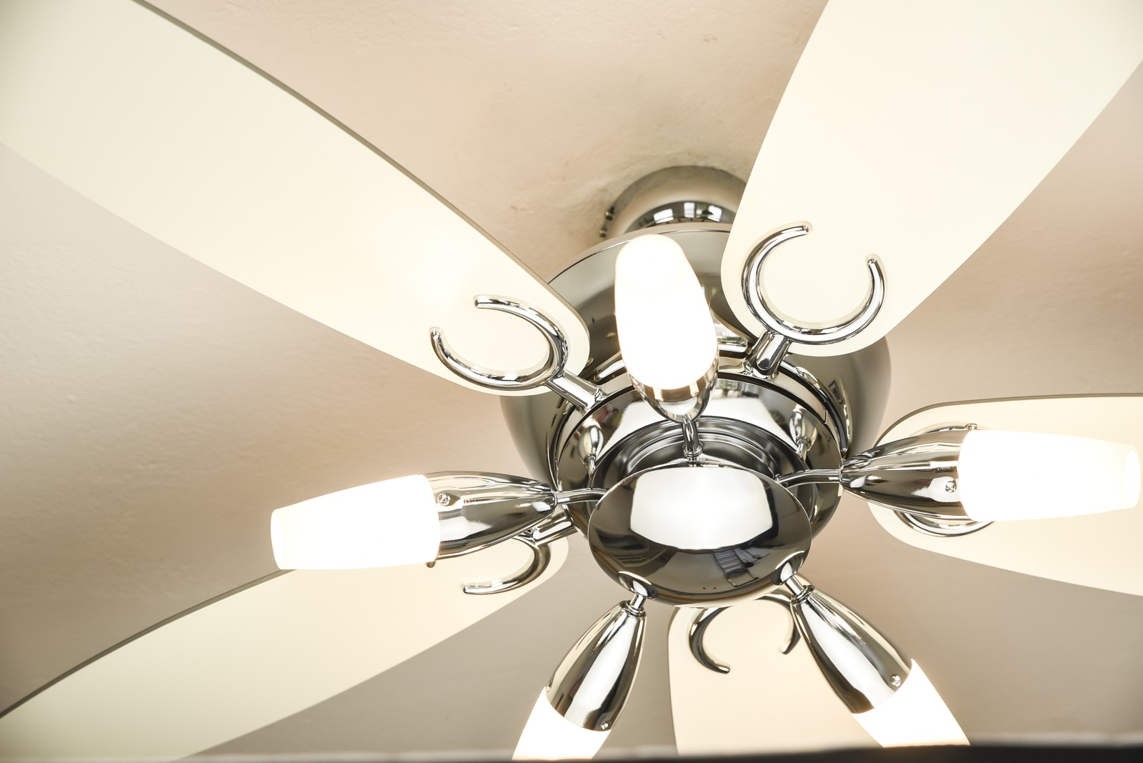 Ein Deckenventilator mit weißen Flügeln und Chromoberfläche. Der Ventilator hat Lichter angebracht.
