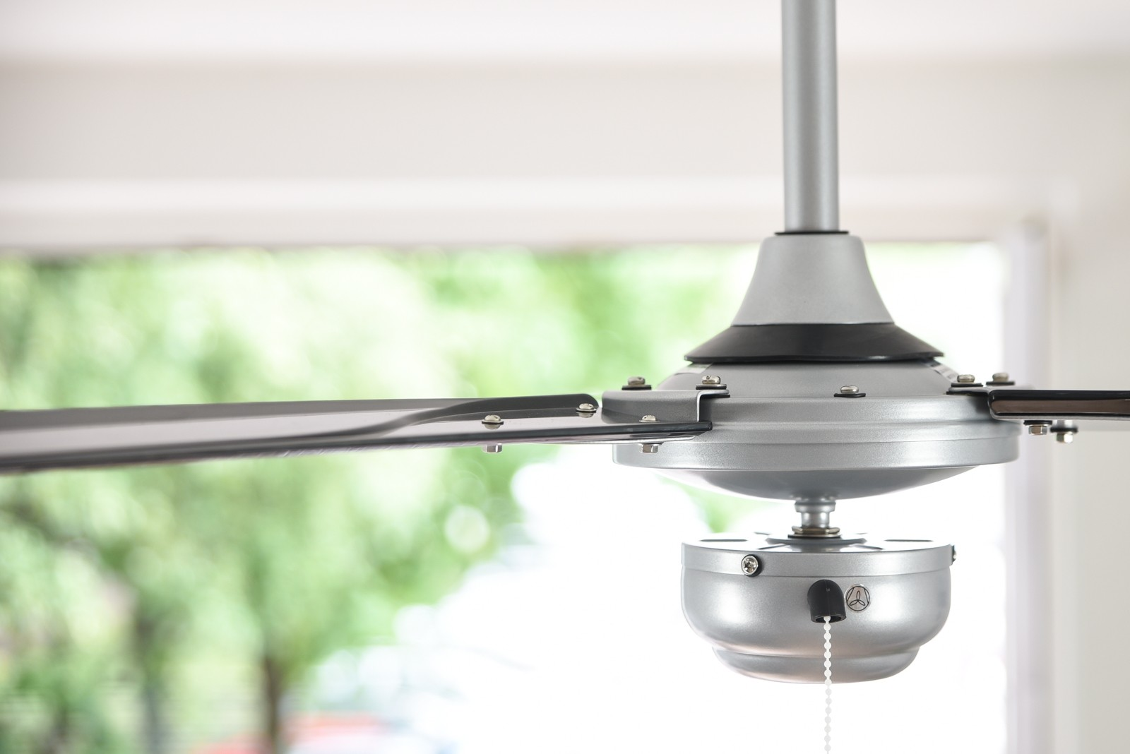Primo piano di un ventilatore da soffitto argentato con 3 pale. Le pale sono grigie e il ventilatore è su sfondo bianco.