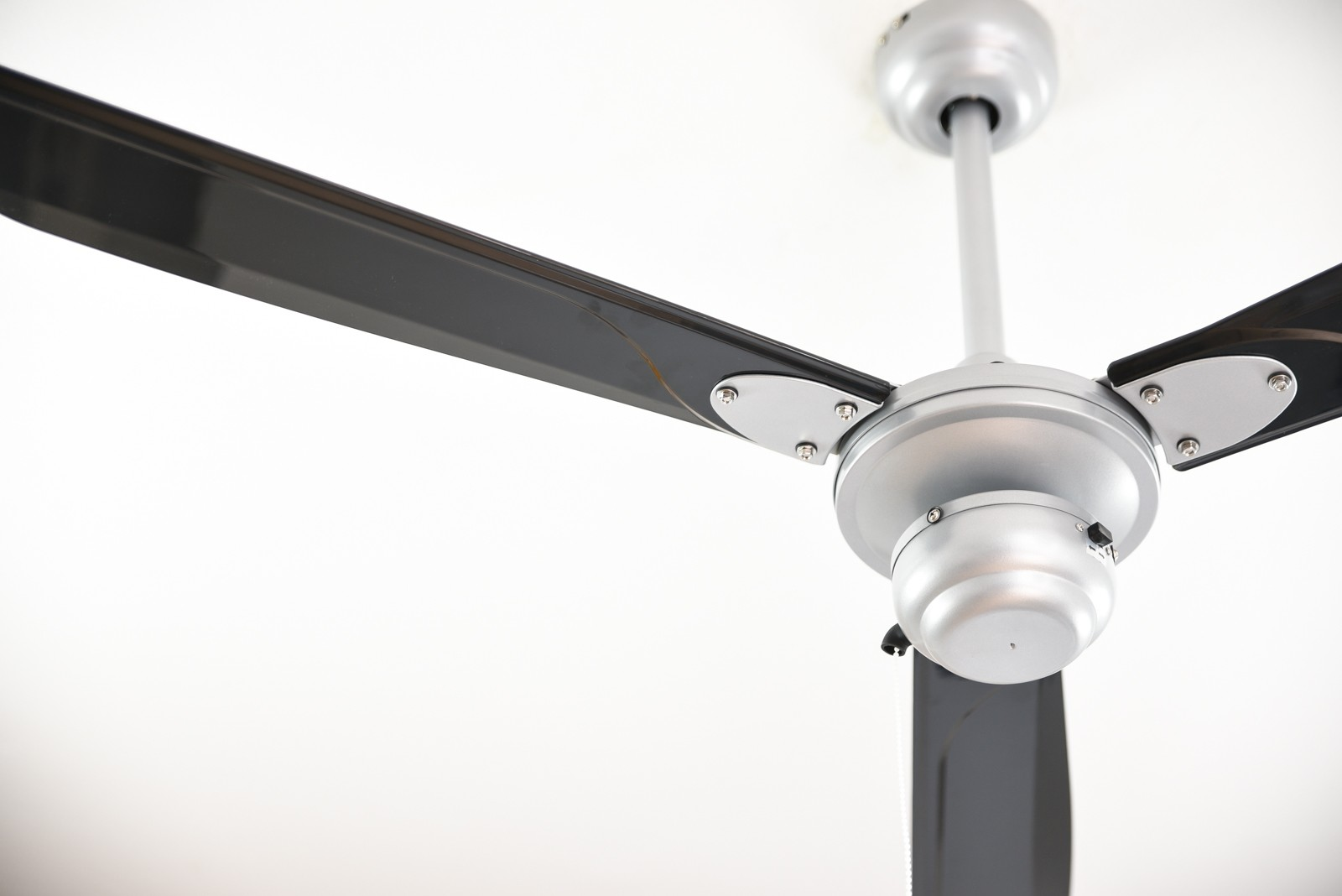 Ventilatore da soffitto argentato con tre pale nere. È montato su un soffitto bianco.