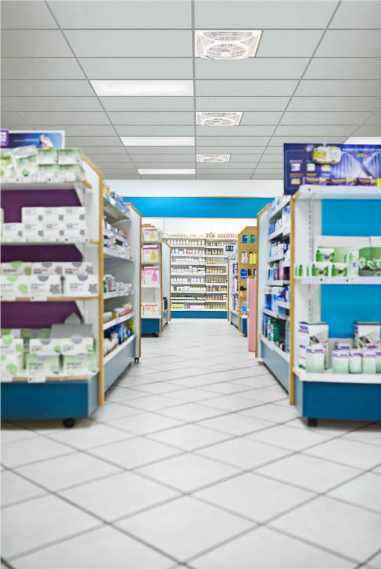Un interno di farmacia con scaffali di prodotti. Gli scaffali sono riforniti. Pavimento e soffitto bianchi. Ben illuminato.