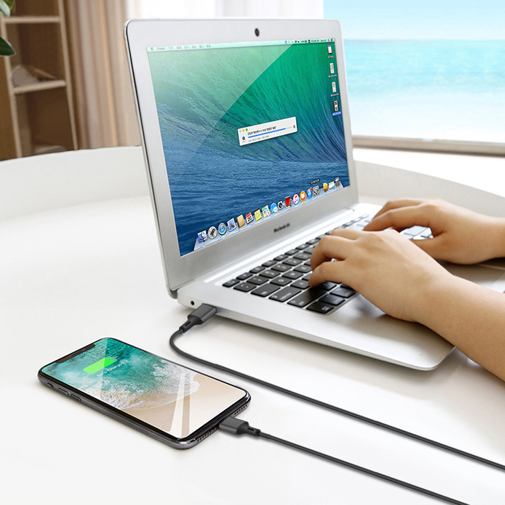 Ein Laptop lädt ein Telefon. Das Telefon befindet sich links und ist über ein Kabel mit dem Laptop verbunden.