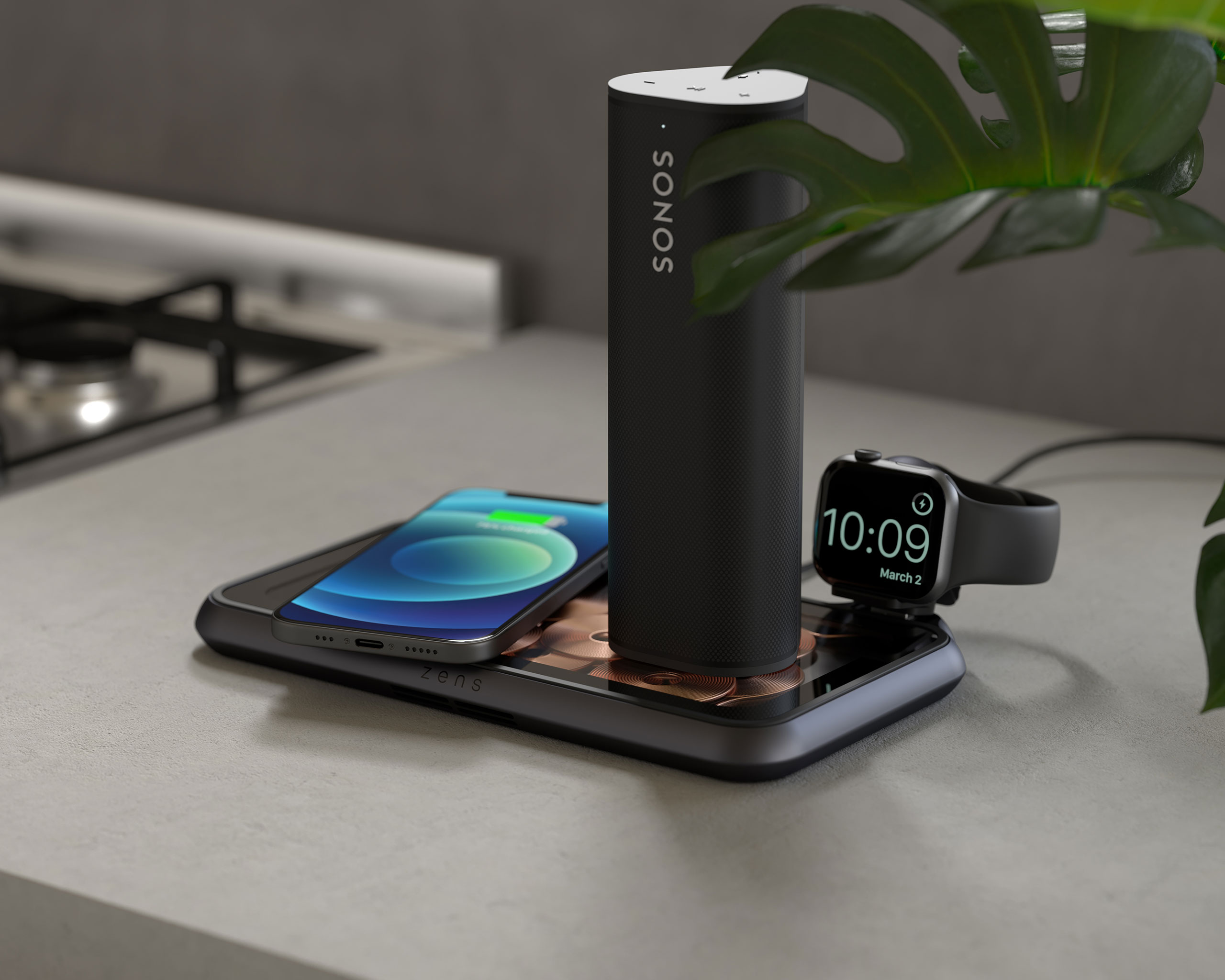 Eine Ladestation mit Telefon, Smartwatch und Lautsprecher. Sie steht auf einer grauen Oberfläche.