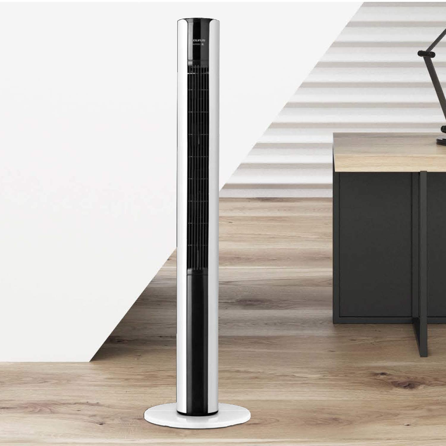 Biało-czarny wentylator wieżowy na drewnianej podłodze. Biała ściana z czarnym biurkiem w tle.