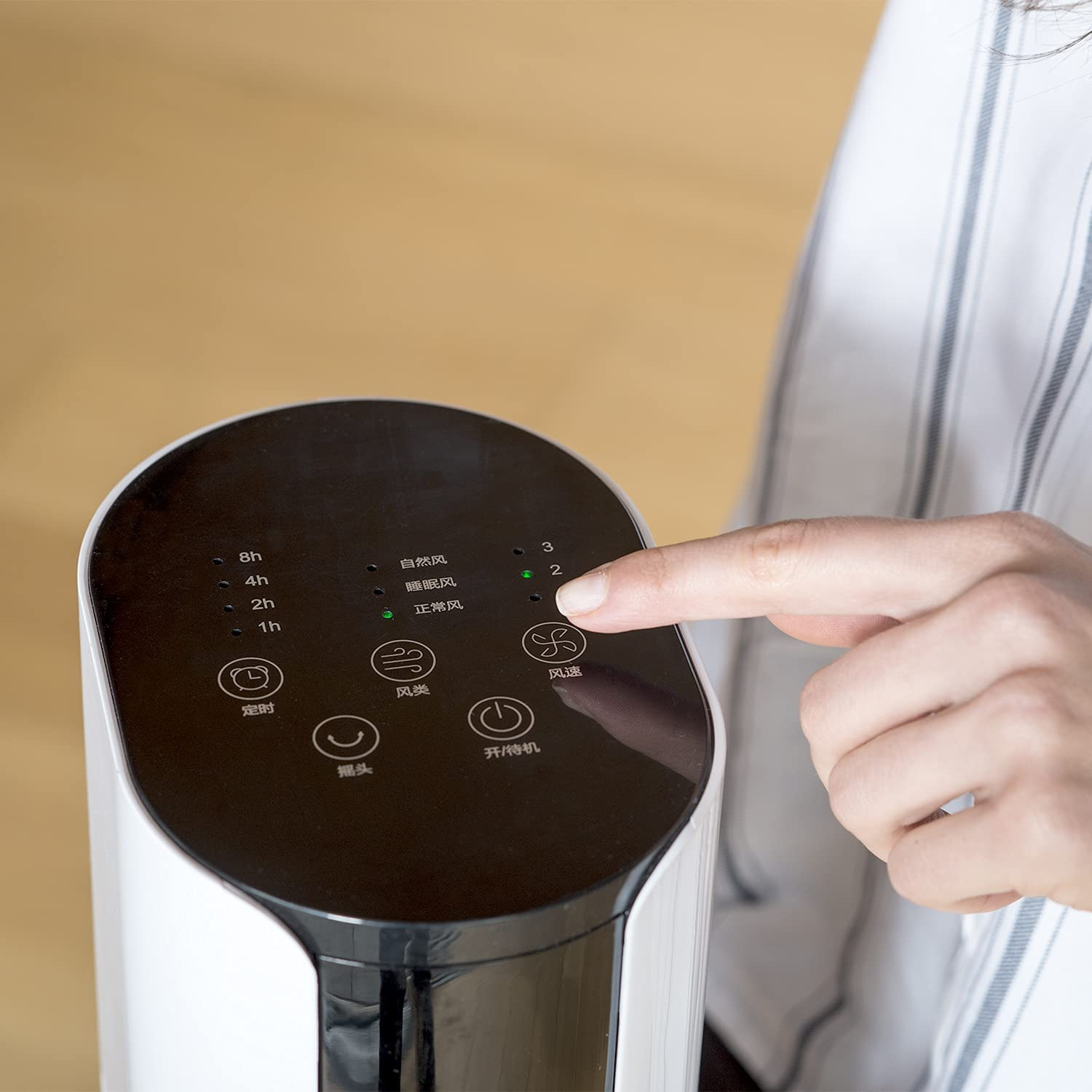 Dłoń osoby wskazująca na panel sterowania białego wentylatora.