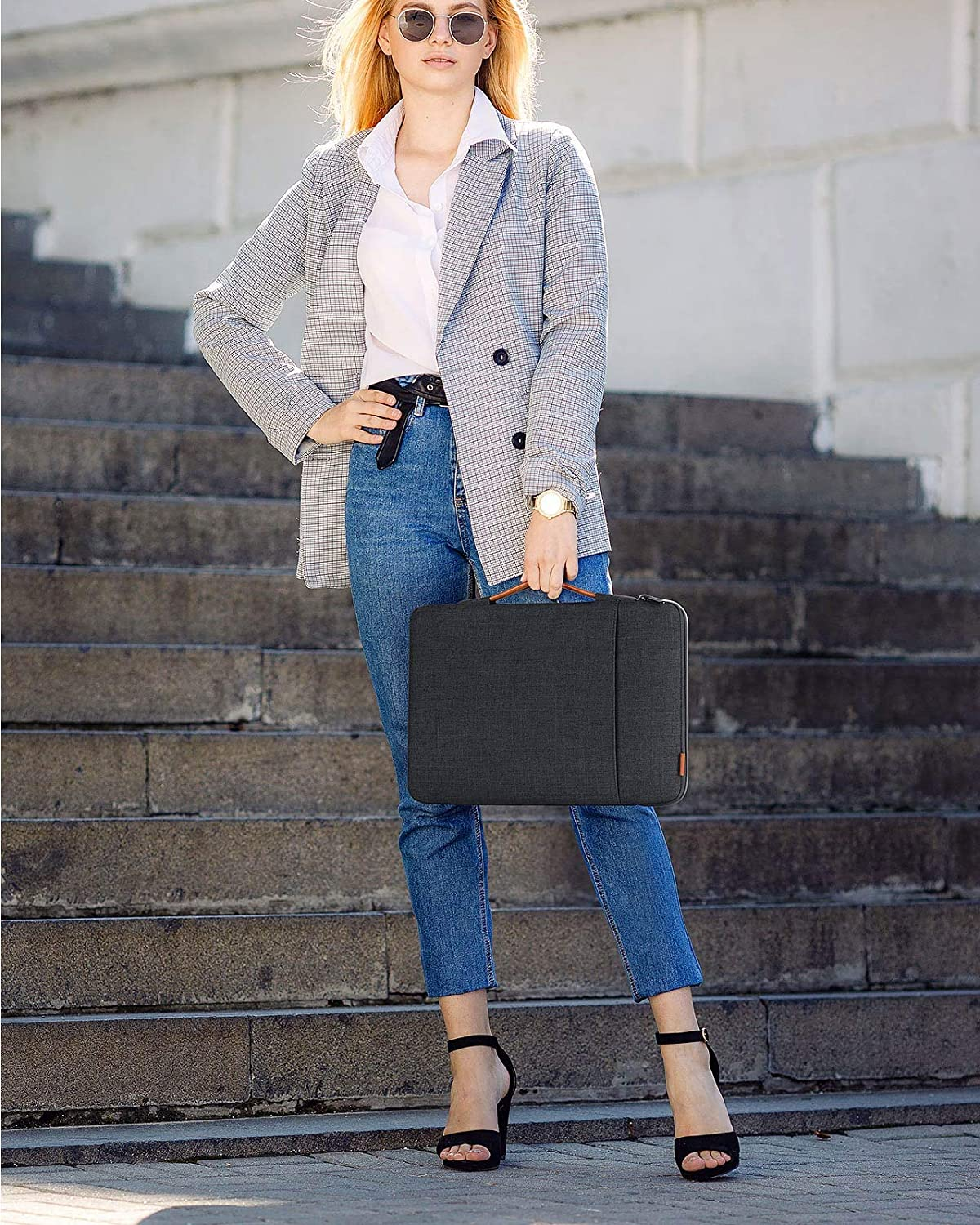 Frau hält eine dunkelgraue Laptoptasche, während sie auf Stufen steht. Sie trägt eine Sonnenbrille.