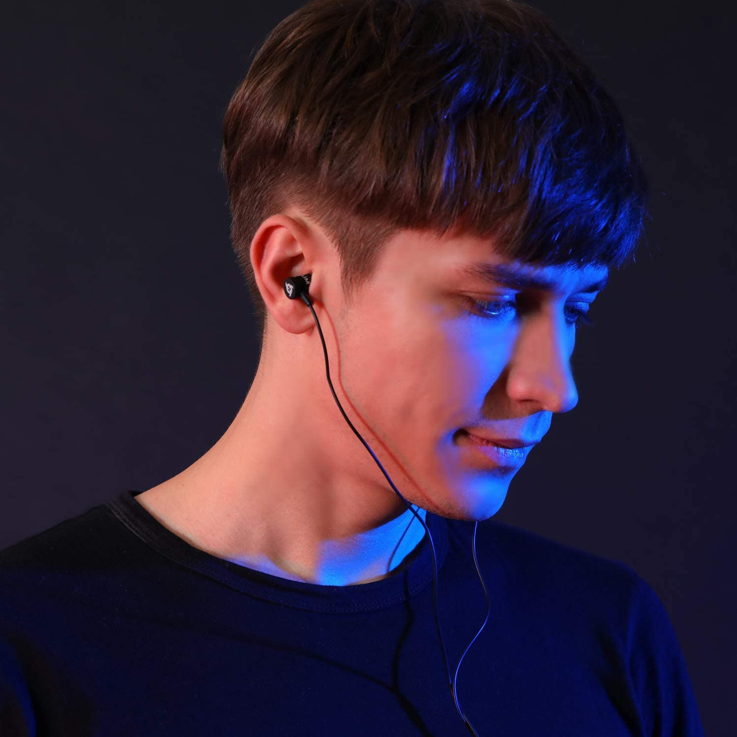 Un uomo con auricolari neri, che guarda in basso, con uno sfondo blu e viola.