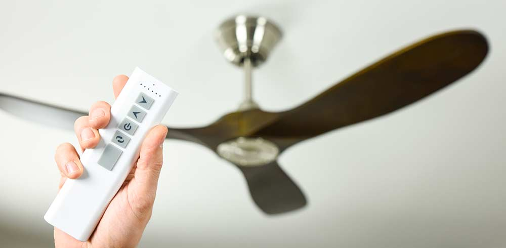 Mano che tiene un telecomando bianco che punta a un ventilatore da soffitto.