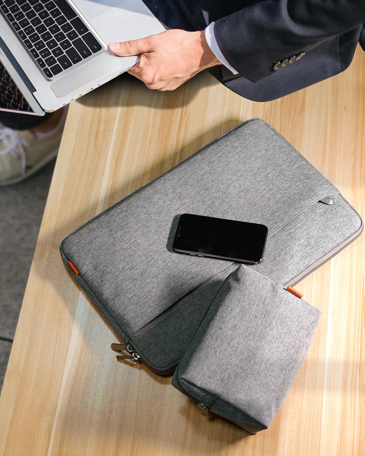 Eine Person benutzt einen Laptop auf einem Holztisch mit Telefon, Hülle und Beutel im Vordergrund.