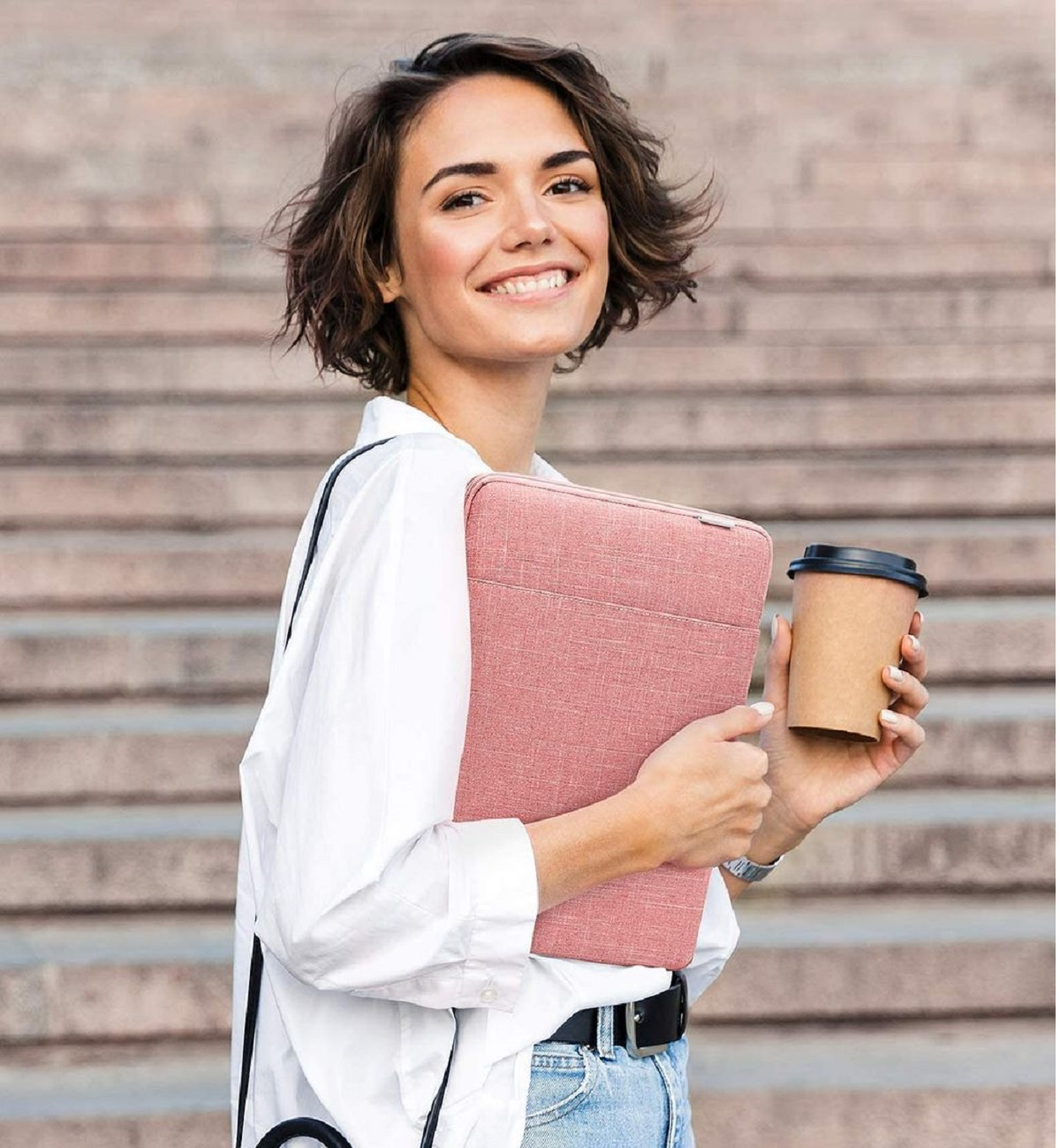Frau hält pinkfarbene Laptoptasche und Kaffeetasse, lächelt auf Treppe.