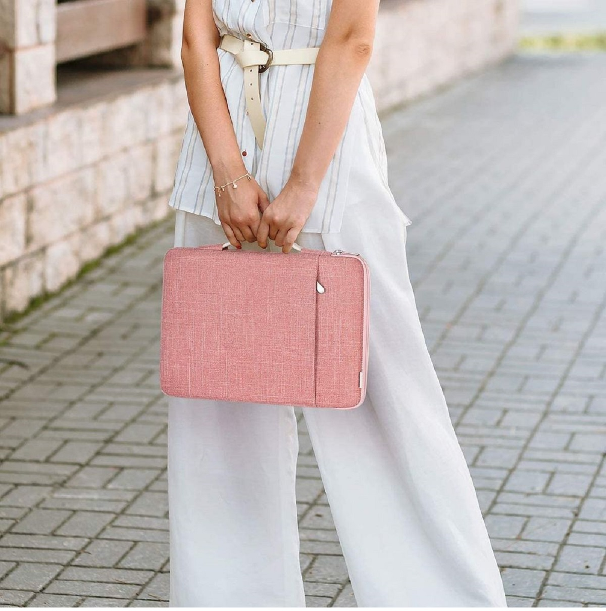 Frau in Weiß hält eine rosa Laptoptasche.  Draußen.