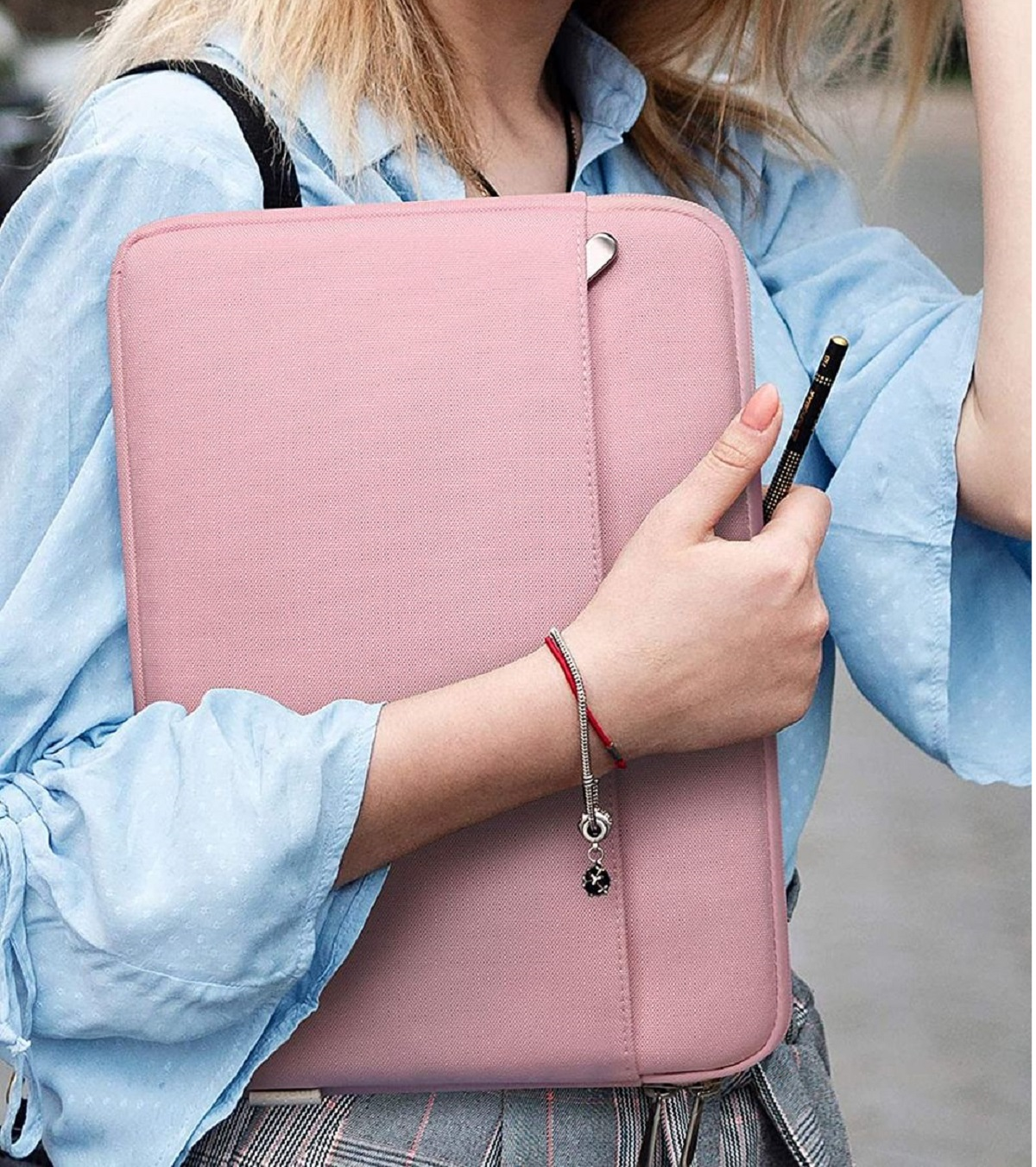 Eine Frau hält eine pinkfarbene Laptop-Hülle, trägt ein blaues Hemd und ein Armband mit Anhängern.