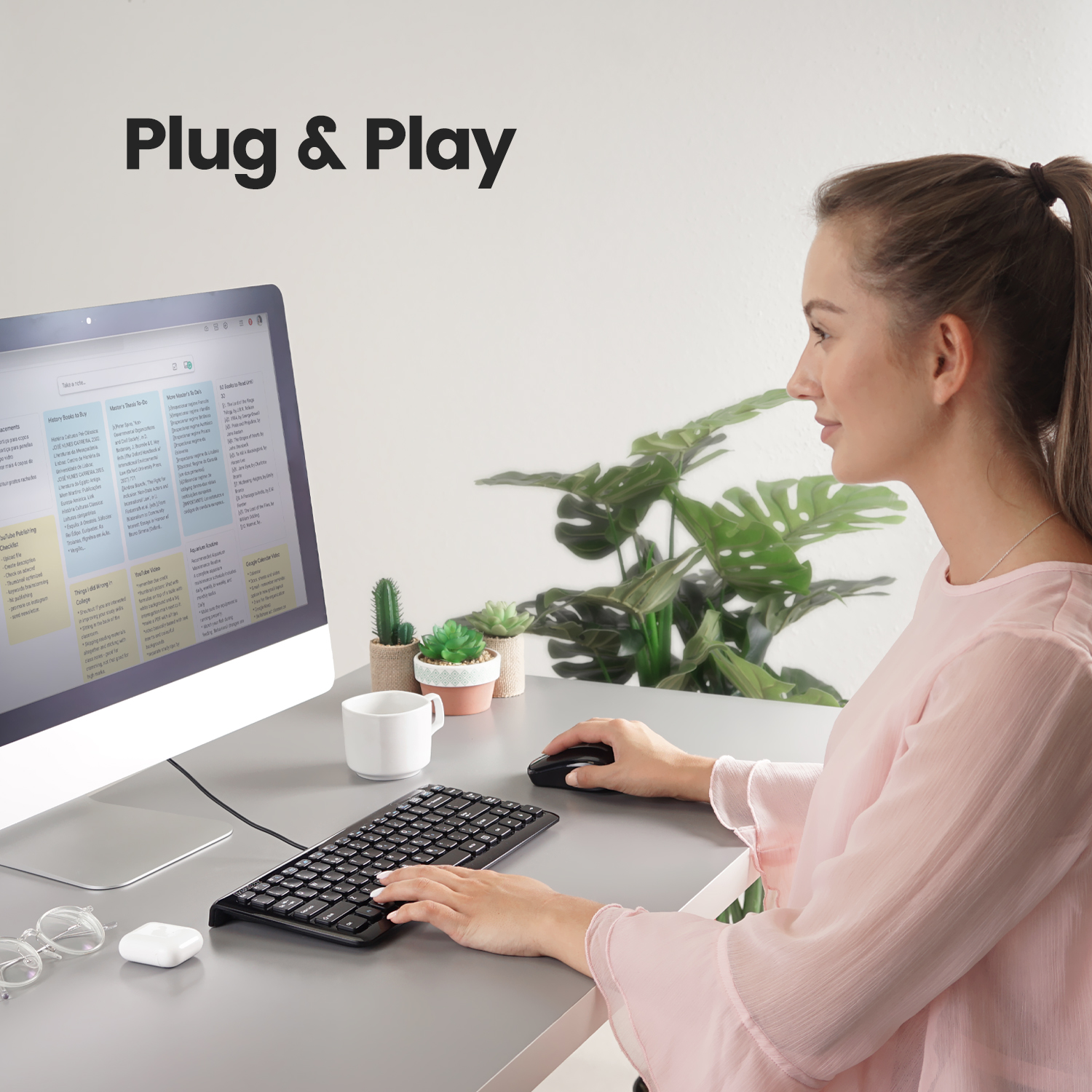Una donna usa tastiera, mouse e monitor neri su una scrivania grigia, con piante sullo sfondo.