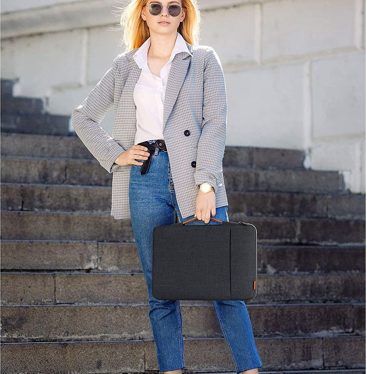 Frau in Jeans und Jacke mit Laptoptasche auf einer Treppe.