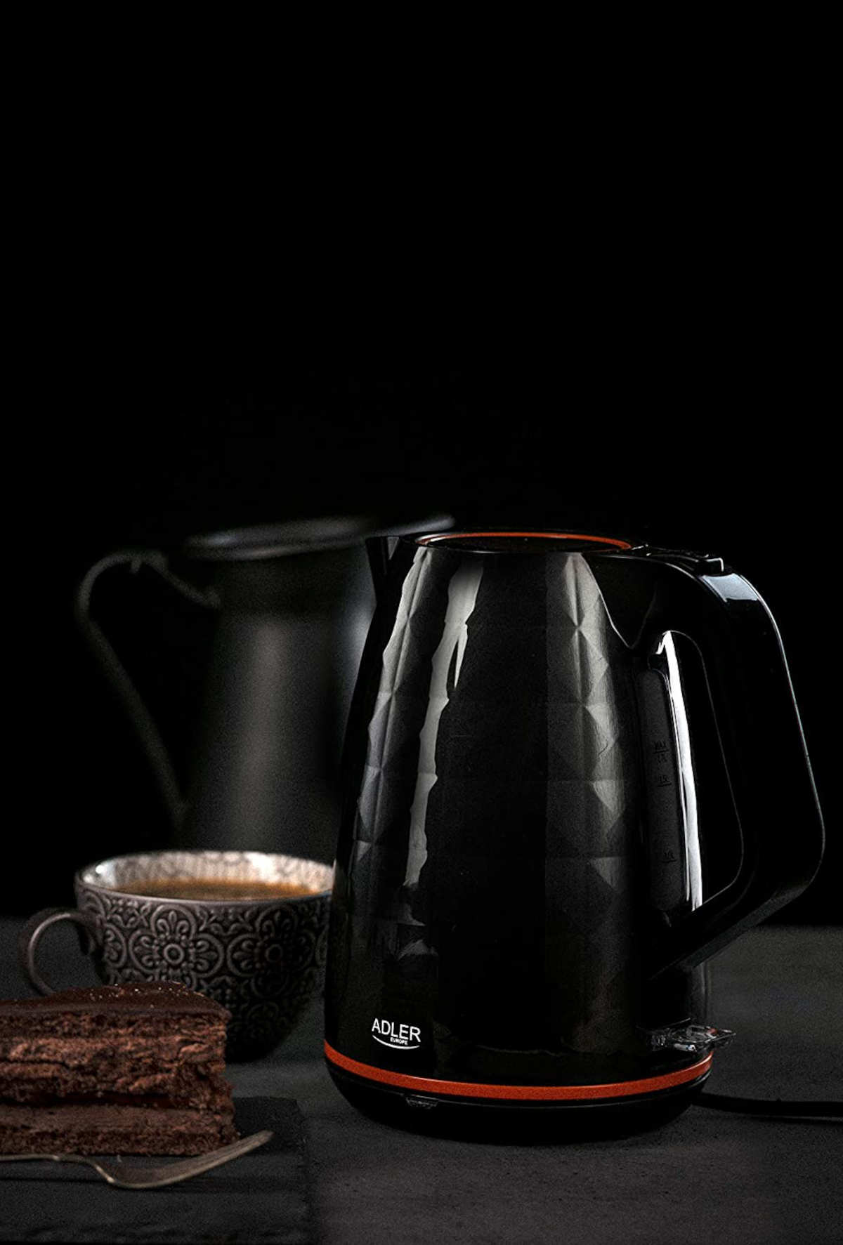 Bouilloire électrique noire. Fond noir. Une théière et un gâteau sur le côté.