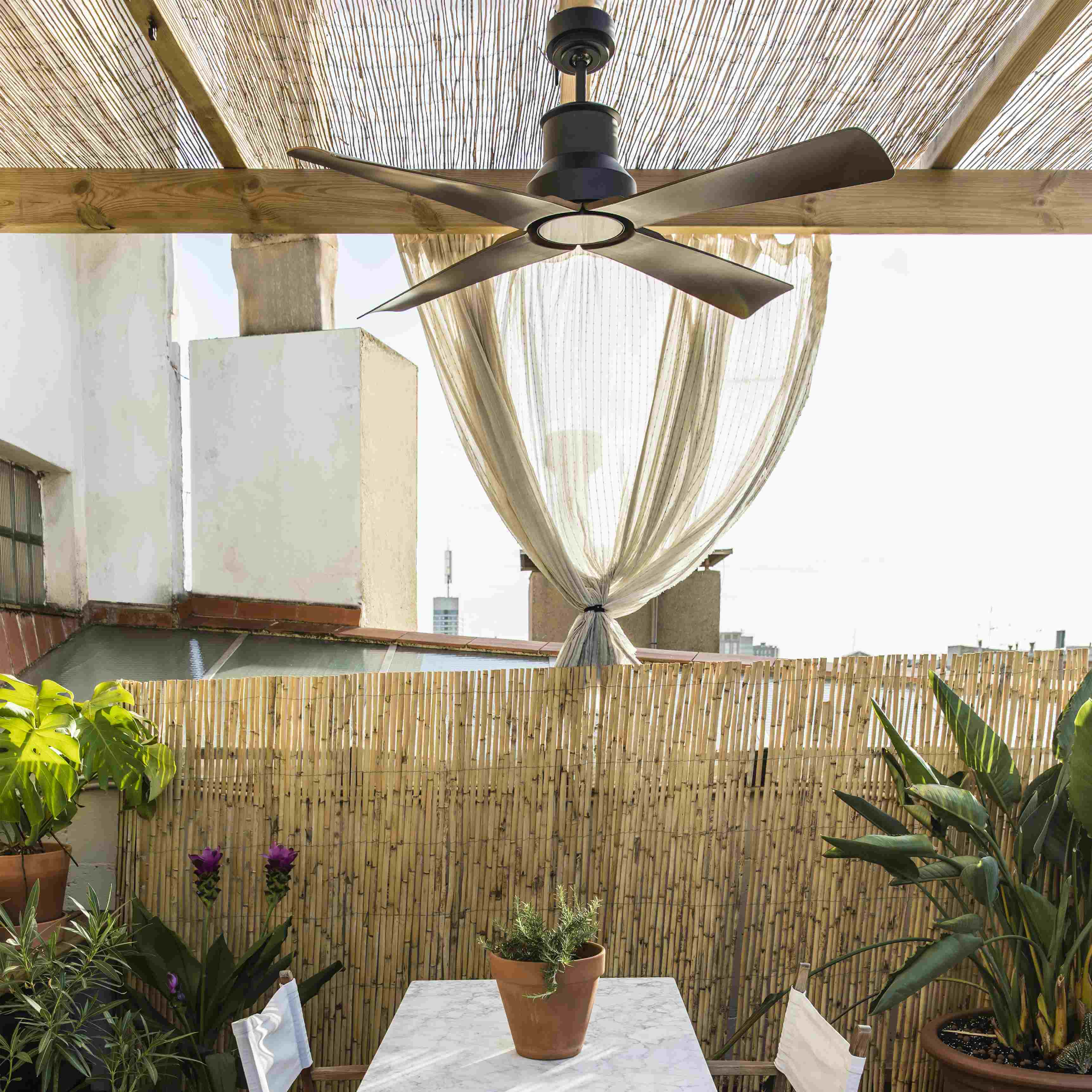 Terrazza sul tetto con recinzione in bambù, piante, ventola e tenda trasparente.