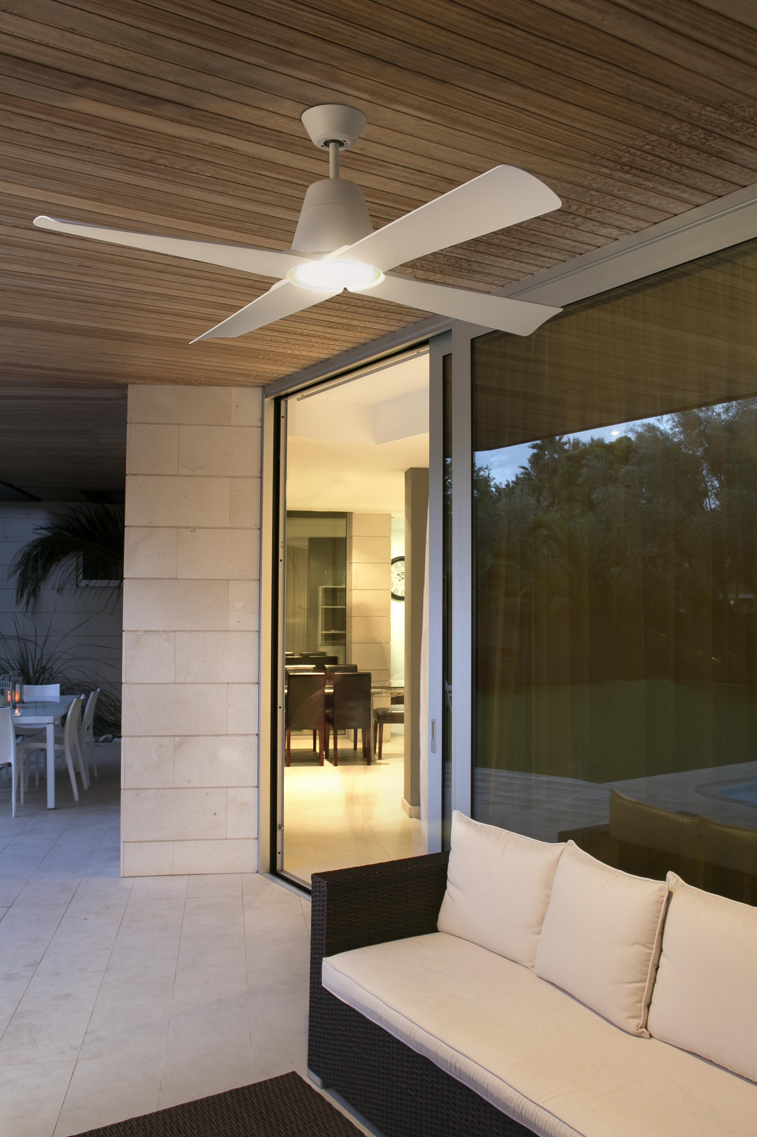 Ventilatore da soffitto bianco con luci su un portico. Divano in primo piano. Porte scorrevoli in vetro.