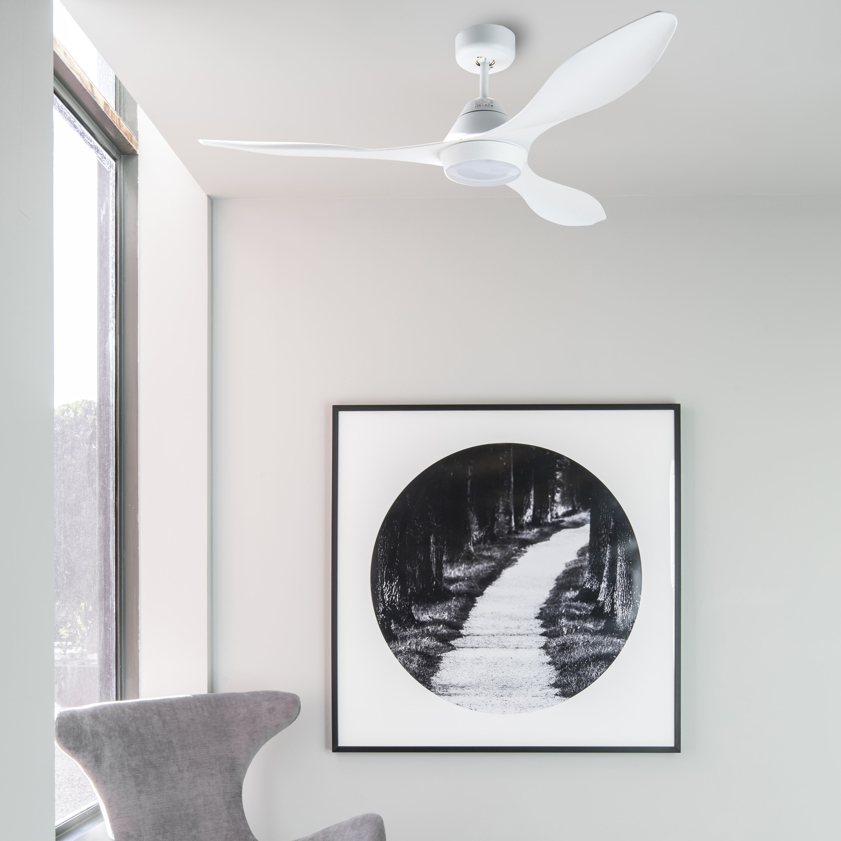 Un ventilatore da soffitto bianco con tre pale si trova in una stanza. Un'immagine incorniciata è appesa al muro.
