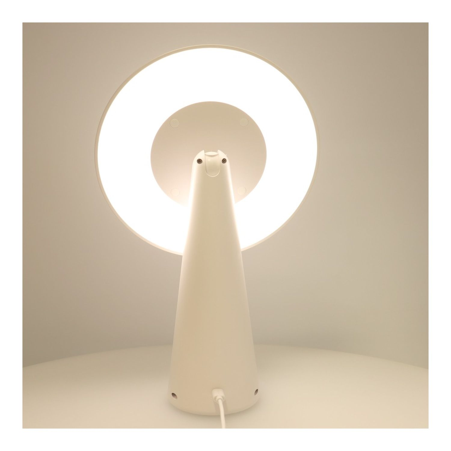 Weiße Tischleuchte mit kreisförmigem Licht. Die Lampe hat eine runde Oberseite und einen konischen Sockel. Auf weißem Grund.