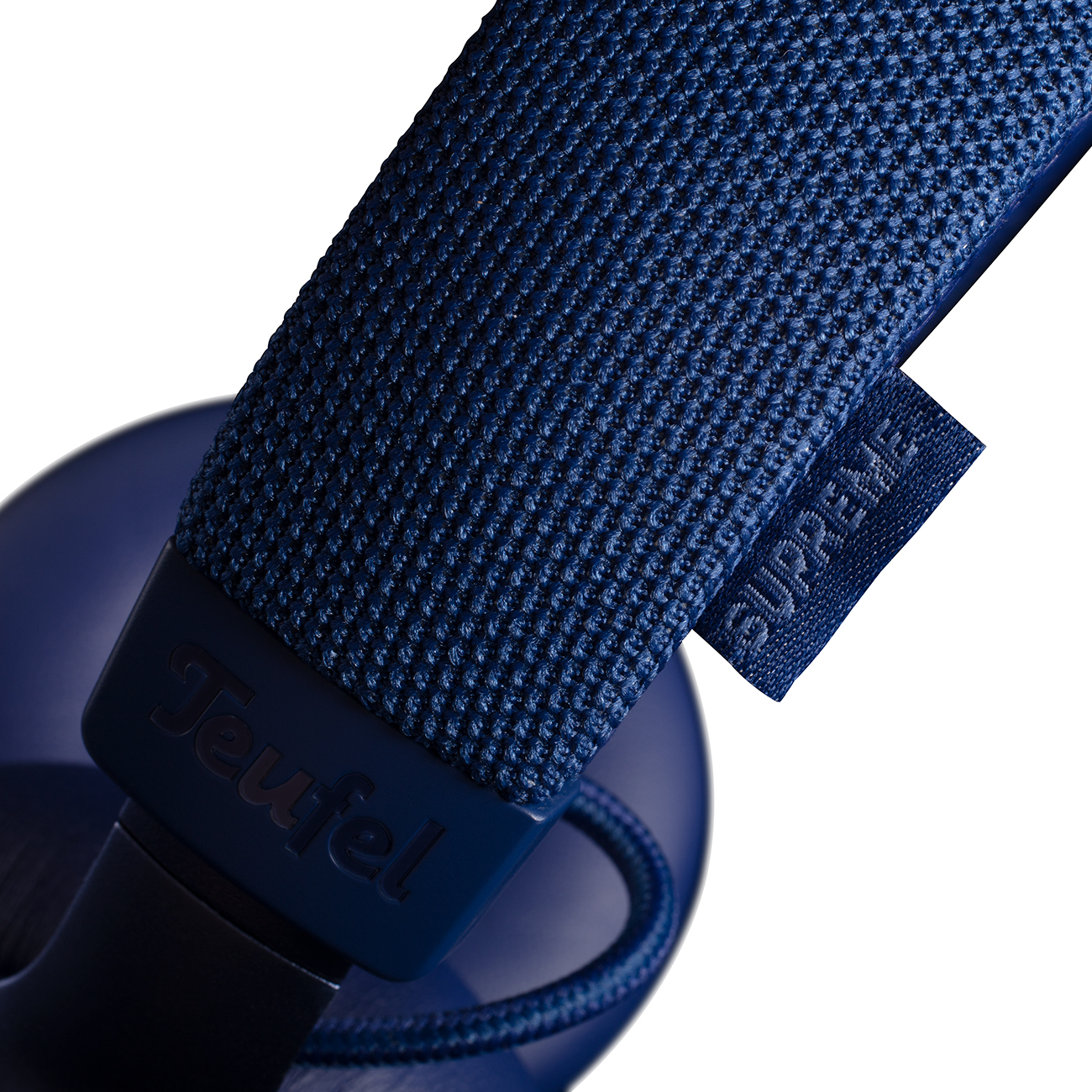 Detalle de auriculares: copa y diadema azul marino. Texto en la diadema, 'SUPREME'.