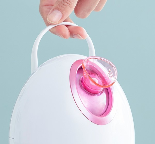 Vaporizzatore facciale bianco con accento rosa e manico. Una mano tiene il manico.