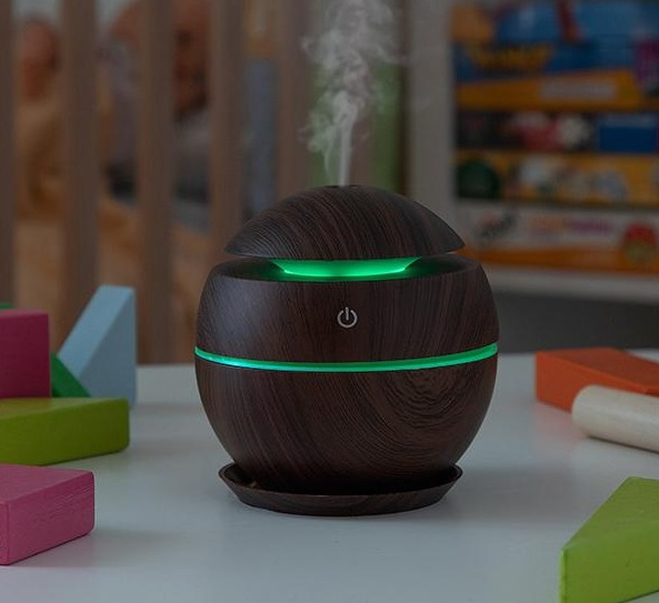 Un difusor de aceites esenciales de color madera oscura con una luz verde y un botón de encendido.