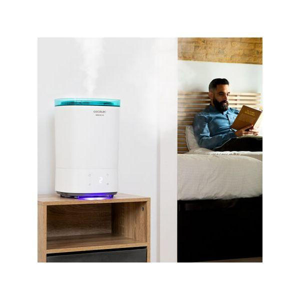 Uomo che legge a letto, vicino a un umidificatore bianco su un comodino di legno, parete bianca.