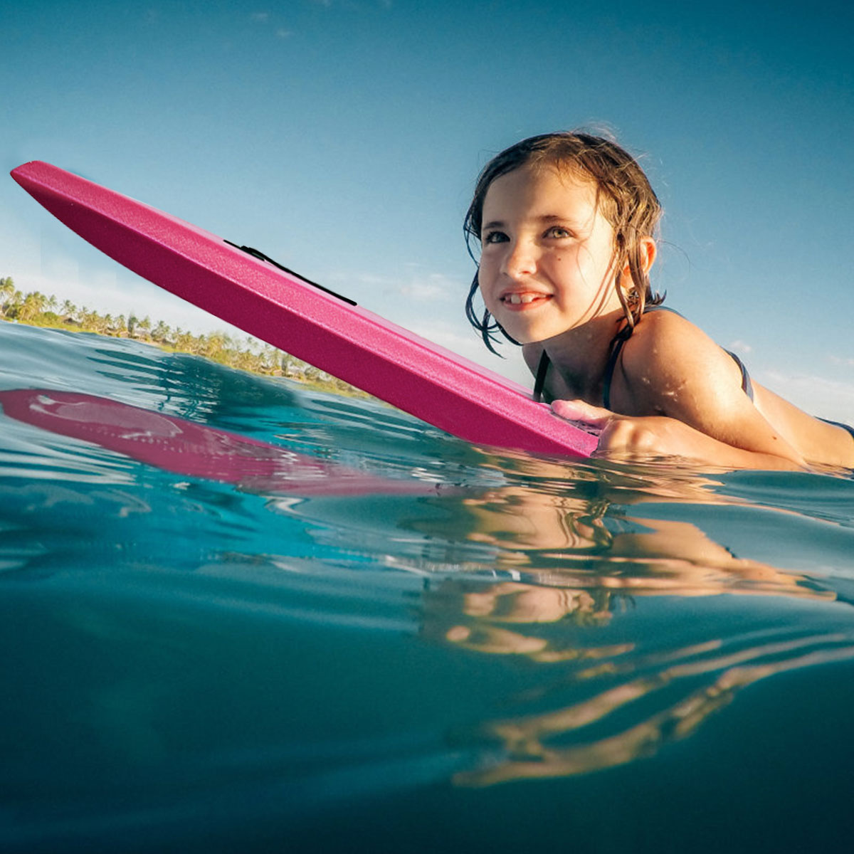 Mädchen auf einem rosa Surfbrett im Meer, das in den Himmel schaut.