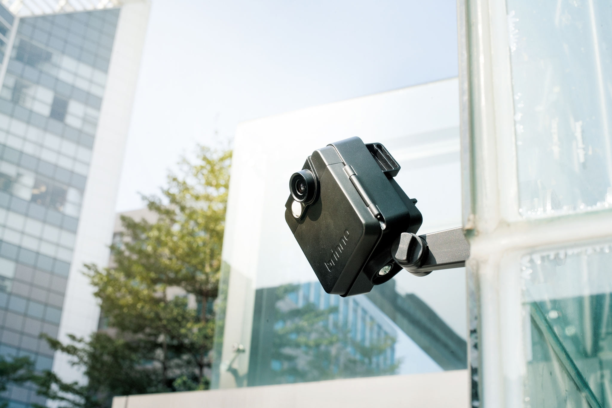 Una telecamera di sicurezza nera montata su un muro di blocchi di vetro, rivolta allo spettatore.