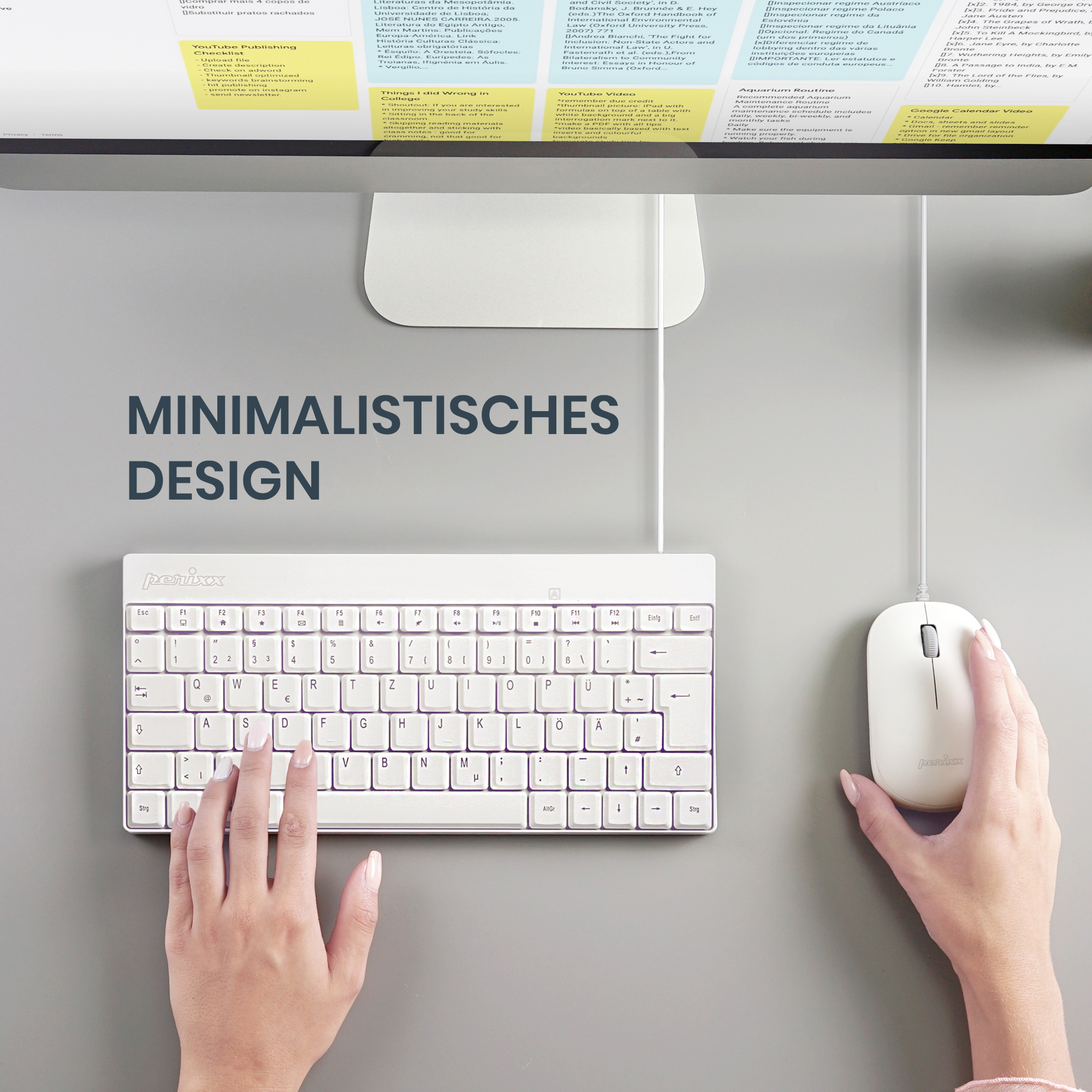 Weiße Tastatur und Maus auf einem grauen Schreibtisch, mit einem Computermonitor im Hintergrund.